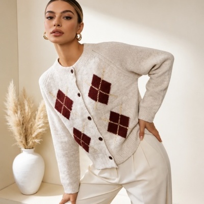 Mulher com cardigan bege e calças brancas em ambiente neutro.
