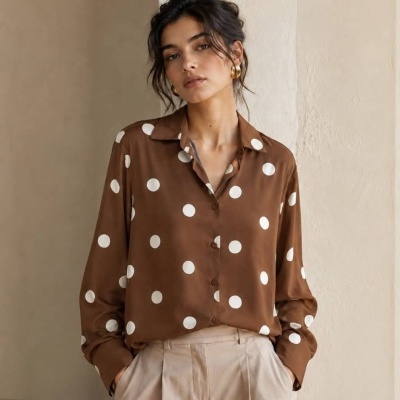 Blusa castanha com bolinhas brancas, calças bege, ambiente interior.
