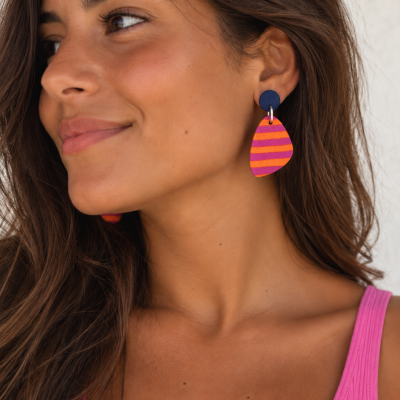 Mulher com brincos triangulares laranja e rosa e peça azul escuro, usando top rosa.