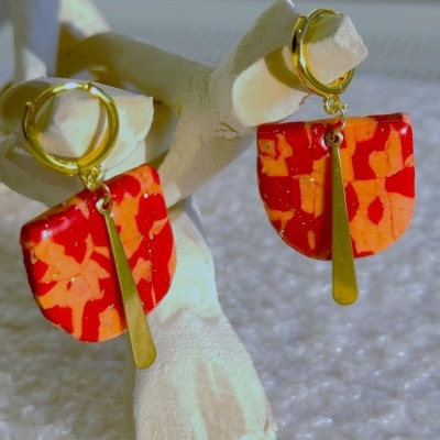 Brincos dourados com pendente semicircular vermelho e laranja em suporte branco