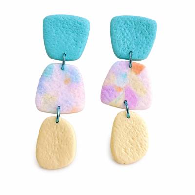 Brincos pendentes em três formas geométricas azuis, multicolor pastel e amarelo claro com textura irregular.