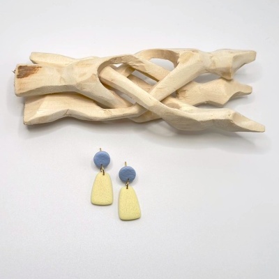 Brincos azul e amarelo claro texturados em superfície branca com peça decorativa dourada clara