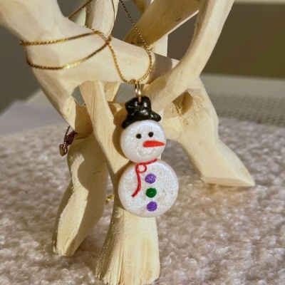 Colar com boneco de neve pendurado em estrutura de madeira clara.