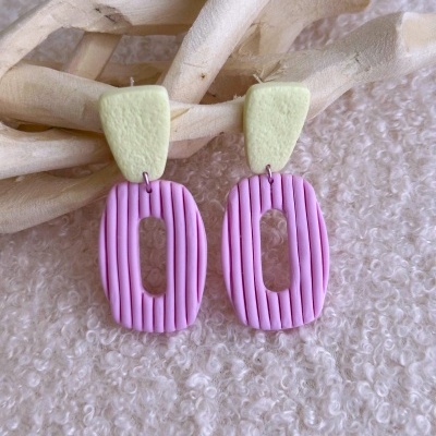Brincos creme e rosa de design oval com linhas verticais apoiados em madeira clara