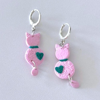 Brincos de gato rosa com coração verde e argolas prateadas sobre fundo branco.
