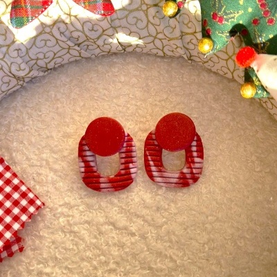 Brincos vermelhos lisos e riscas vermelhas e brancas sobre tecido branco felpudo com decoração natalícia