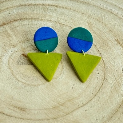 Brincos geométricos em azul, verde escuro e verde claro sobre fundo de madeira clara