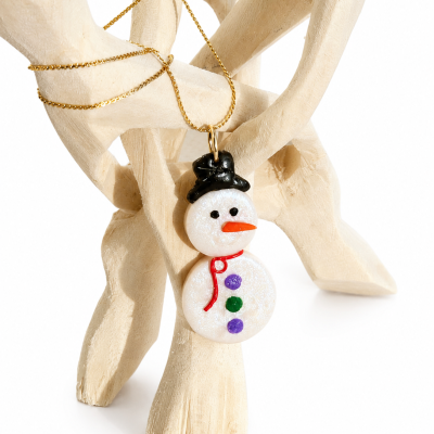 Colar com pendente de boneco de neve brilhante com detalhes coloridos e chapéu preto numa escultura de madeira clara