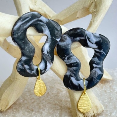 Brincos pretos marmoreados com pendente dourado pendurados em estrutura de madeira