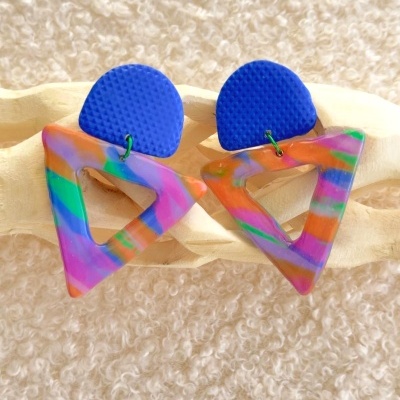 Brincos triangulares coloridos com base azul texturizada.