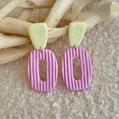 Brincos coloridos em fundo texturizado claro com galho decorativo