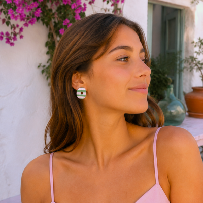 Brincos ovais verdes e brancos com ponto castanho usados por mulher com vestido rosa