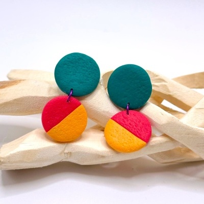 Brincos redondos em argila colorida com verde água, rosa e amarelo, sobre objeto decorativo de madeira clara