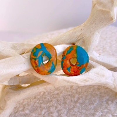 Brincos redondos laranja e azul com buraco, sobre estrutura de madeira