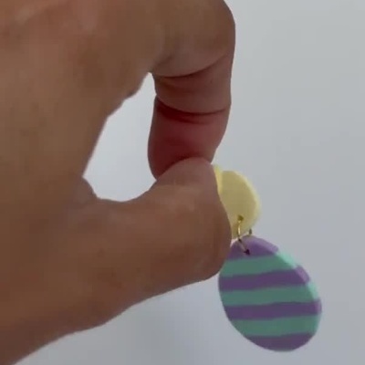 Brinco artesanal amarelo com pingente redondo roxo e azul listrado e coração amarelo.