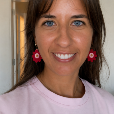 Mulher com brincos de flores vermelhas e camisa rosa em fundo interior branco