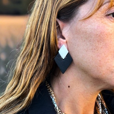 Brincos em forma de losango branco e preto usados por mulher com colar metálico