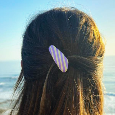 Presilha de cabelo riscada roxa e amarela em cabelo castanho junto ao mar
