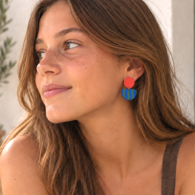 Brincos vermelhos e azuis com riscas verdes usados por mulher com cabelo castanho claro