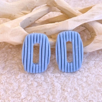 Brincos ovais azuis com textura riscada sobre superfície branca texturizada