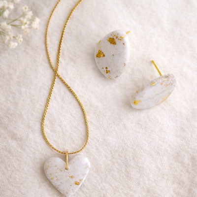 Colar e brincos branco com detalhes dourados sobre tecido bege.