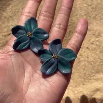 Flores artificiais azuis escuras numa mão em fundo de areia
