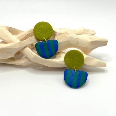 Par de brincos verdes e azuis com padrão de riscas sobre madeira clara