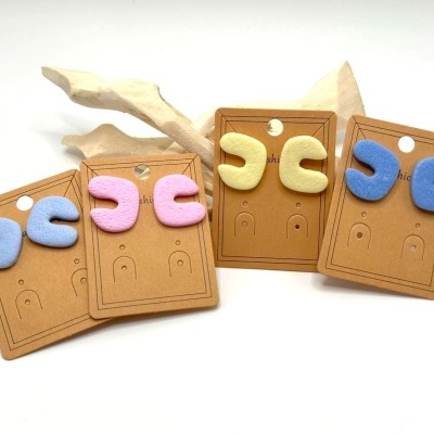 Brincos de argola em azul, rosa, amarelo e azul escuro em cartões castanhos com decoração de madeira clara.