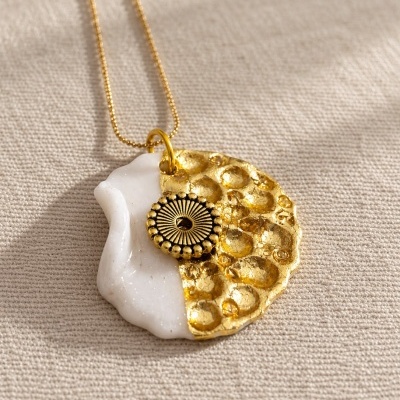 Colar com pendente redondo metade branco metade dourado com textura e detalhe circular dourado.