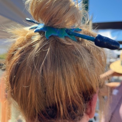 Grampo azul de cabelo segurando coque loiro sob sol.
