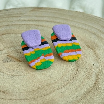 Brincos coloridos com padrão irregular em base de madeira clara.