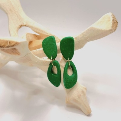 Brincos verdes pendentes em forma orgânica sobre estrutura de madeira clara
