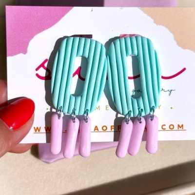 Brincos ovais azuis claros com penduricalhos rosa em cartão de apresentação.