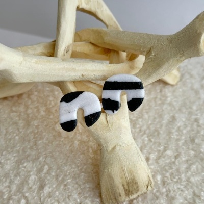 Brincos pretos e brancos em forma de U sobre estrutura de madeira clara