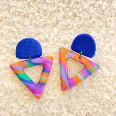 Brincos coloridos com formas geométricas sobre tecido felpudo claro