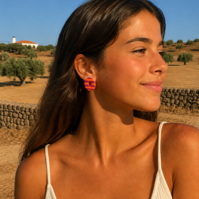 Brincos redondos rosa e laranja com padrão riscado usados por mulher com top branco num ambiente ao ar livre.