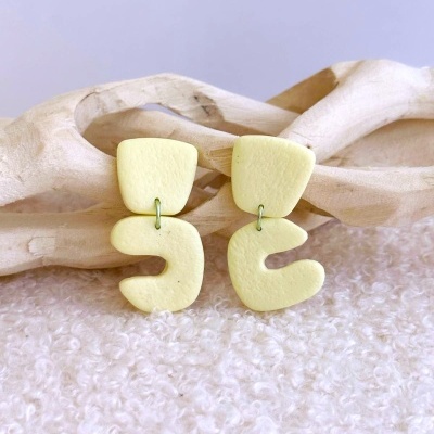 Brincos amarelos pastéis abstratos pendurados em peça de madeira clara