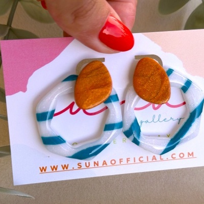 Brincos geométricos laranja e listrados, em cartão com texto www.sunaoofficial.com