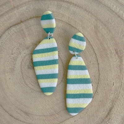 Brincos com riscas horizontais em verde, branco, amarelo e azul sobre fundo de madeira clara.