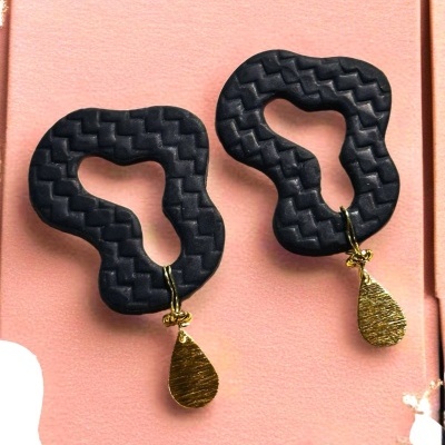 Brincos pretos com textura ziguezague e pendentes dourados em fundo cor-de-rosa