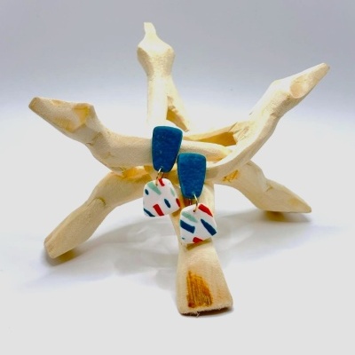 Brincos azuis com pendentes brancos coloridos numa peça de madeira clara