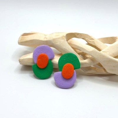 Brincos coloridos com camadas verde, laranja e lilás sobre pedra de madeira entrelaçada