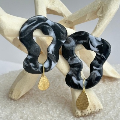 Brincos abstratos em resina preta com padrões brancos e pendentes dourados em forma de gota