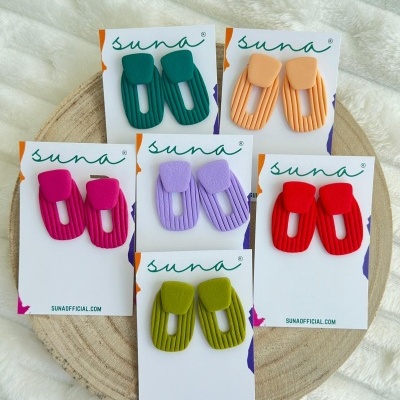 Cinco pares de brincos coloridos em cartões brancos com a marca suna.