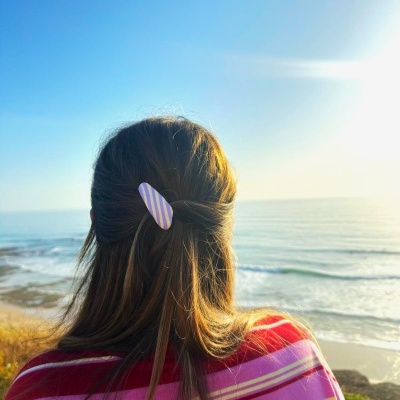 Pessoa com cabelo preso por presilha às riscas e camisola às riscas junto ao mar