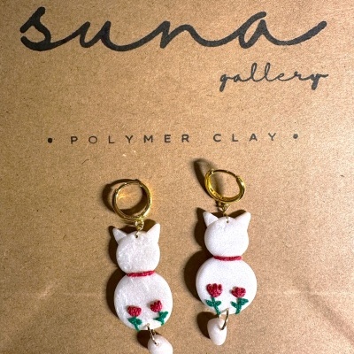 Brincos de gato em argila polimérica branca com flores vermelhas e argolas douradas sobre cartão