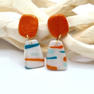 Brincos artesanais laranja e branco com riscas coloridas em fundo branco e galhos de madeira