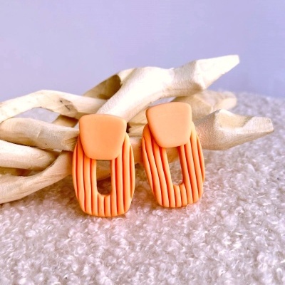 Brincos laranja de resina com textura e forma geométrica sobre fundo felpudo e ramos de madeira clara