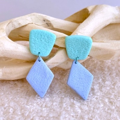 Brincos pendentes azuis com formas geométricas sobre tecido e madeira.