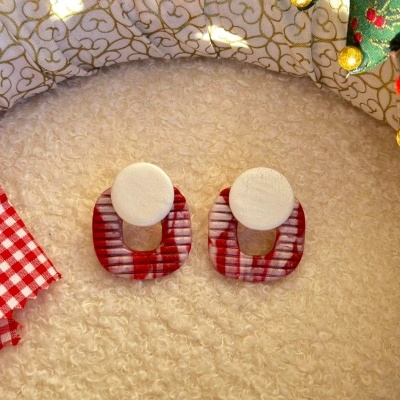 Par de brincos com disco branco e peça ovalada vermelha e branca sobre superfície creme felpuda